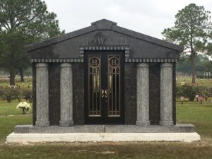 Custom granite walk-in mausoleum with grey granite columns and bronze doors sitting on a concrete foundation.